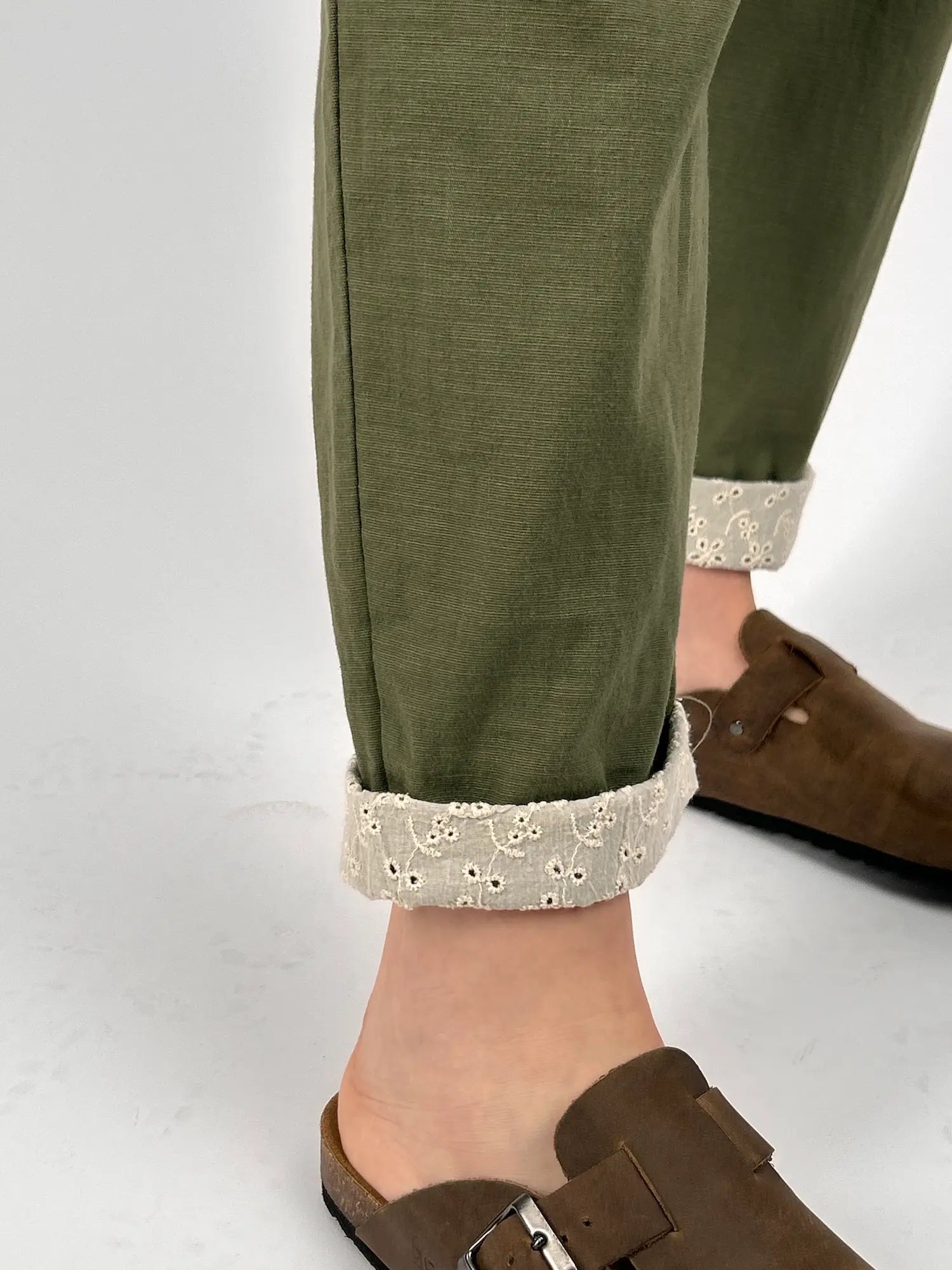 Pantalone donna verde con vita elastica e dettaglio ricamato sul fondo indossato con sabot marroni.. dettaglio risvolto