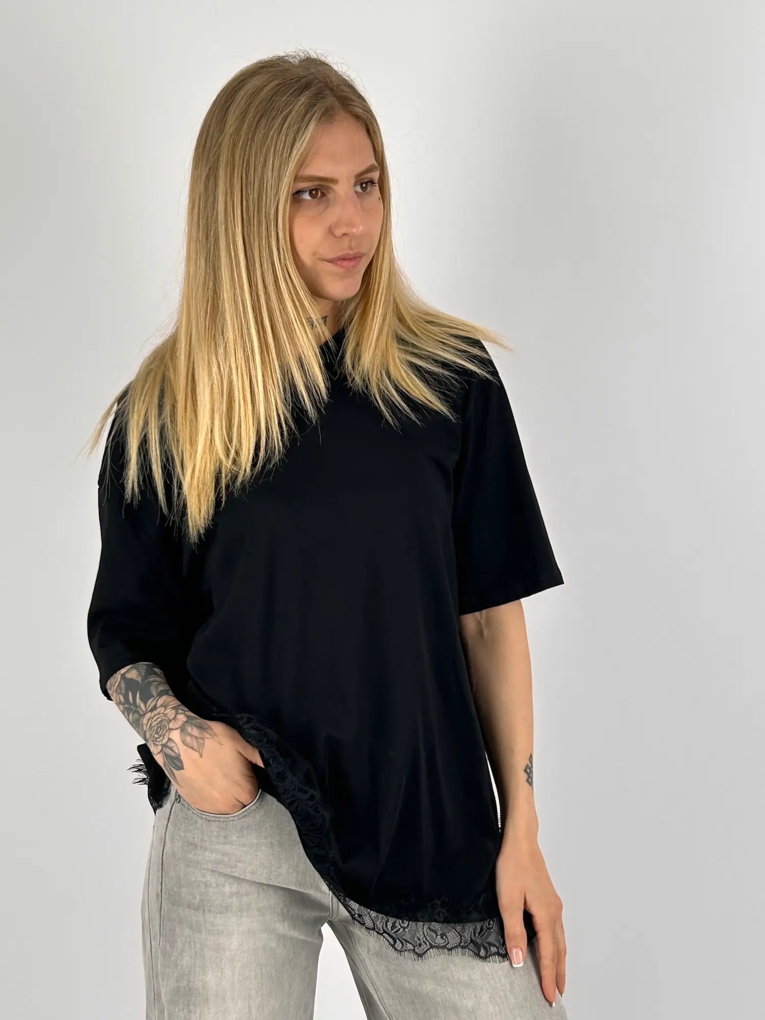T-shirt donna nera over con dettaglio in pizzo sul fondo indossata con jeans chiari. vista frontale