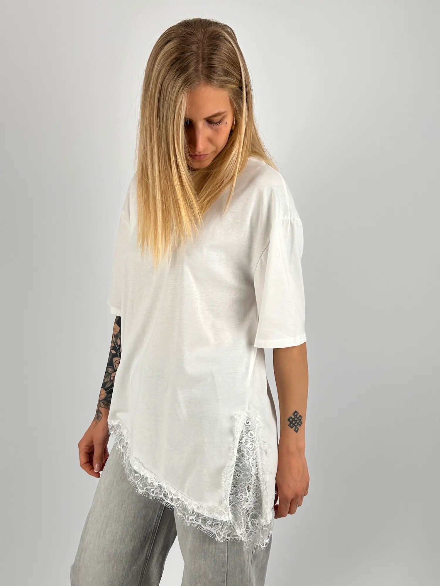 T-shirt donna bianca over con dettaglio in pizzo sul fondo indossata con jeans chiari. vista frontale